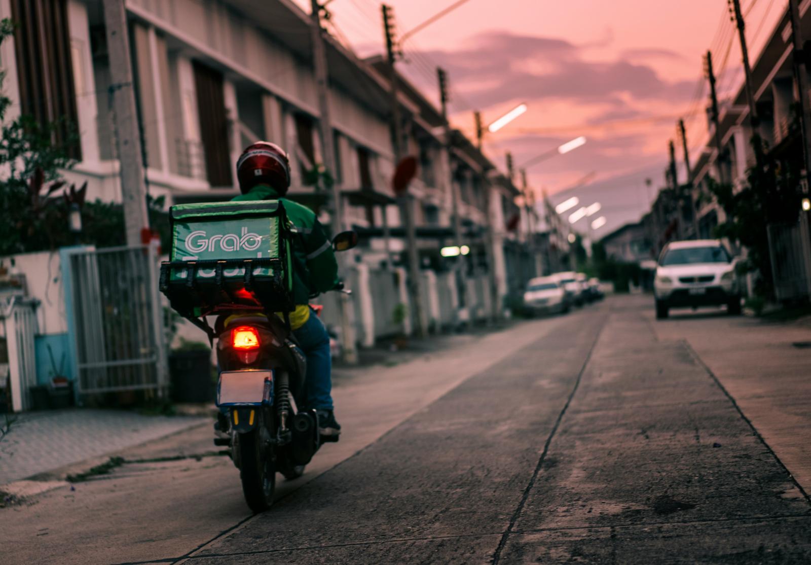 Una persona in moto con in spalla un contenitore per la consegna di cibo a domicilio